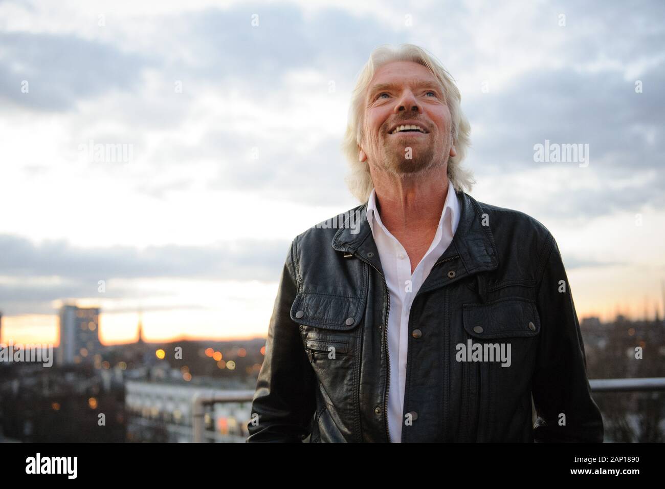 Sir Richard Branson in einer schwarzen Lederjacke und einem weißen, tiellosen Hemd, das vom Dach des Virgin HQ in London zum Himmel blickt. Stockfoto