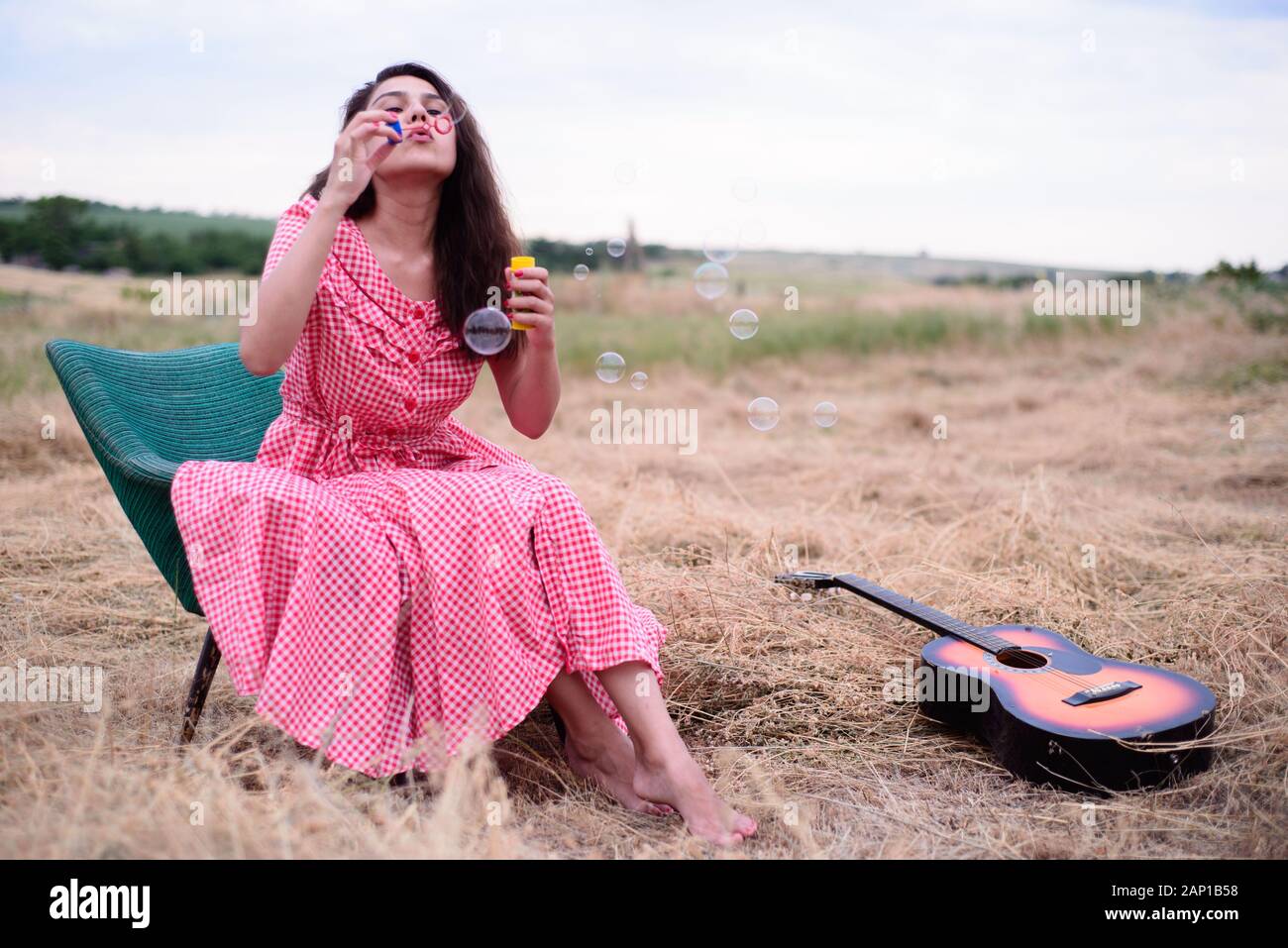 Porträt einer schönen jungen Mädchen, brünett, in einem rot-karierten Kleid, in einem Vintage Sessel sitzt, in das Feld ein. Fänge Seifenblasen, lächelt. Rus Stockfoto