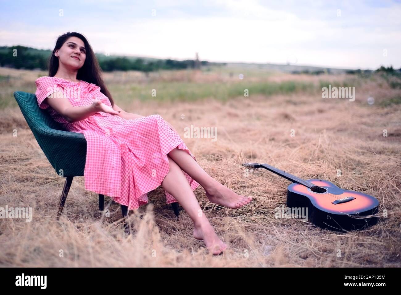 Porträt einer schönen jungen Mädchen, brünett, in einem rot-karierten Kleid, in einem Vintage Sessel sitzt, in das Feld ein. Fänge Seifenblasen, lächelt. Rus Stockfoto