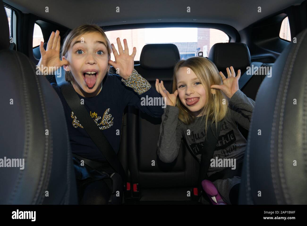 Zwei Kinder auf dem Rücksitz eines Autos, die lustige Gesichter machen Stockfoto