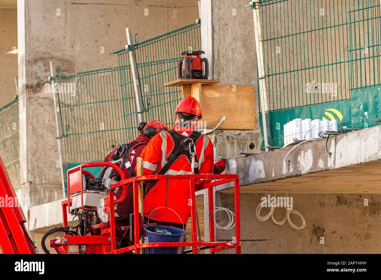 Zwei männliche Bauarbeiter mit roten Schutzhelmen am Kopf und Sicherheitskleidung führen eine Inspektion auf einem Betonboden eines Gebäudes unter Stockfoto