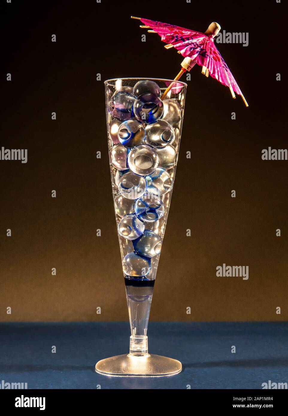 Eine Champagnerflöte gefüllt mit Wasserrückhalteperlen, die wie kugelförmige Eiswürfel aussehen, plus einen Cocktailschirm - kühle Sommergetränke - Kopierraum. Stockfoto