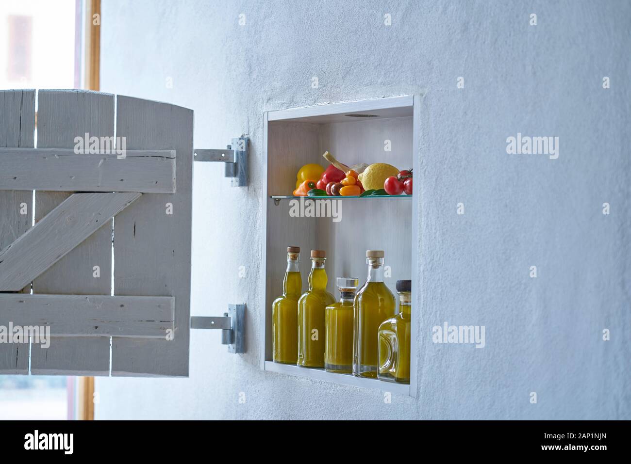 Kleines Regal mit Verschluss an der Wand mit Flaschen Flasche Olivenöl und Gemüse Tomaten Zitronenpaprika und Knoblauch, altes Hausapartment modernes Wohnen Stockfoto