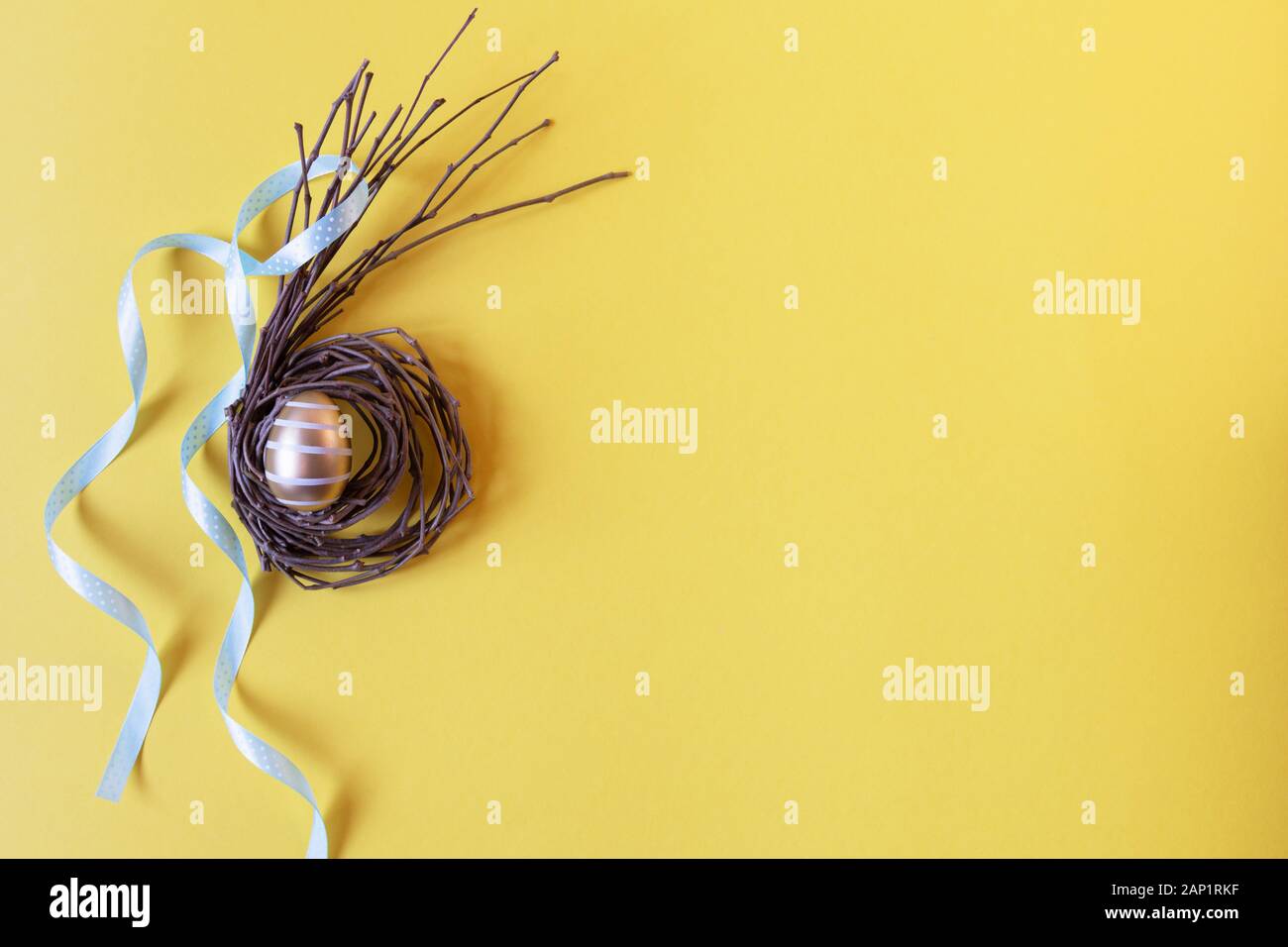 Goldene Osterei auf kreative Nest mit Band auf gelben Hintergrund der Ansicht von oben. Frohe Ostern. Kreative Osterdekoration. Kopieren Sie Platz. Stockfoto