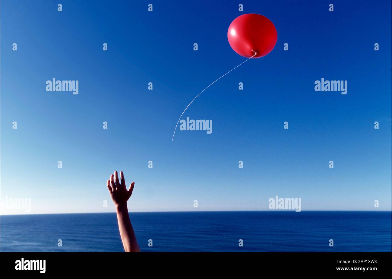 Ein Junge, der seinen roten Ballon über den Atlantik loslässt, gibt dem Ballon die Freiheit Stockfoto