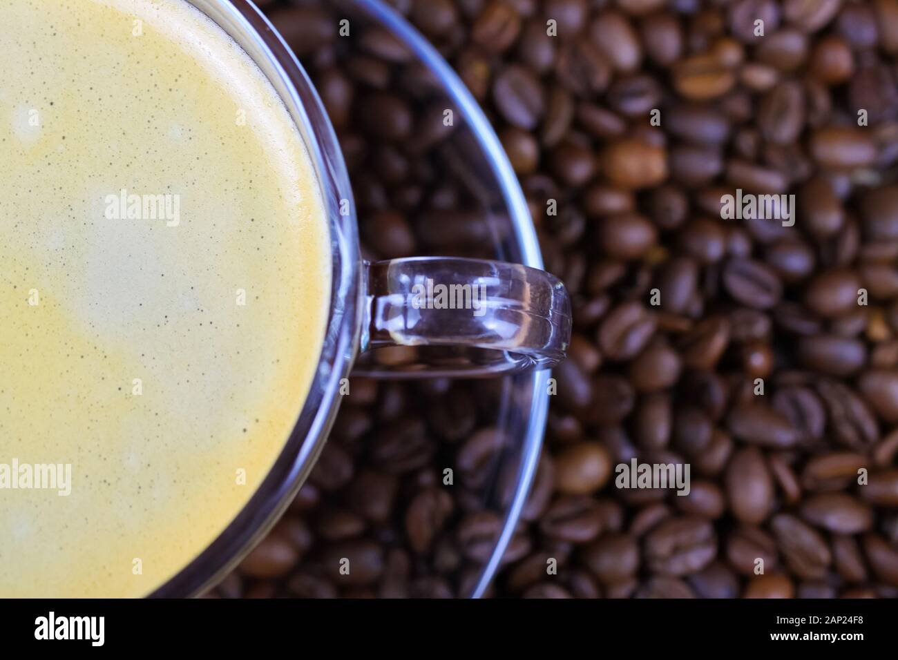 Isolierte halb transparente Kaffee Tasse griff auf Glas Untertasse mit Cafe Crema auf unzähligen gerösteten Bohnen verschwommenen Hintergrund Stockfoto