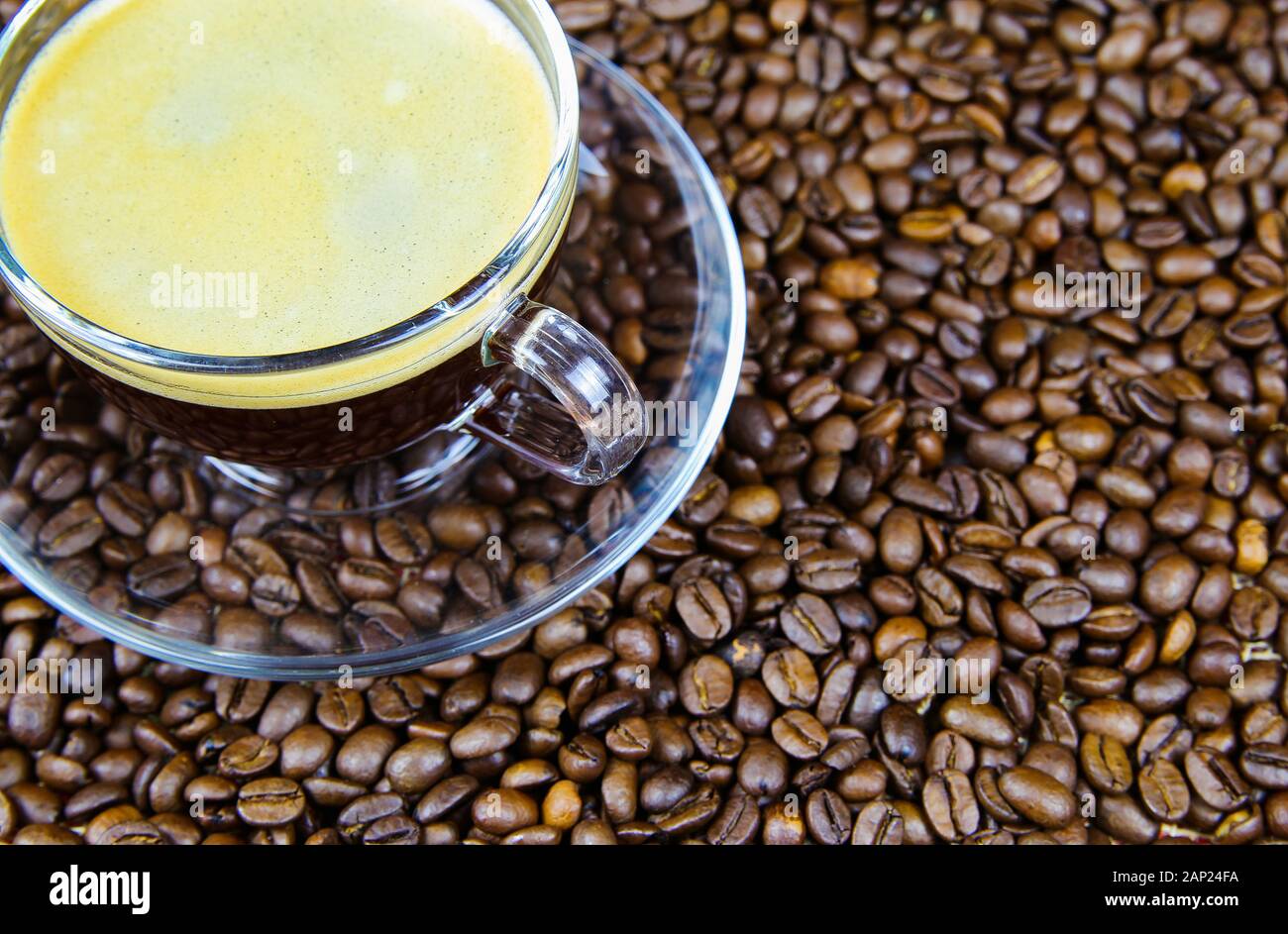 Isolierte transparente Kaffeetasse auf Glas Untertasse mit Cafe Crema auf unzähligen gerösteten Bohnen Hintergrund Stockfoto
