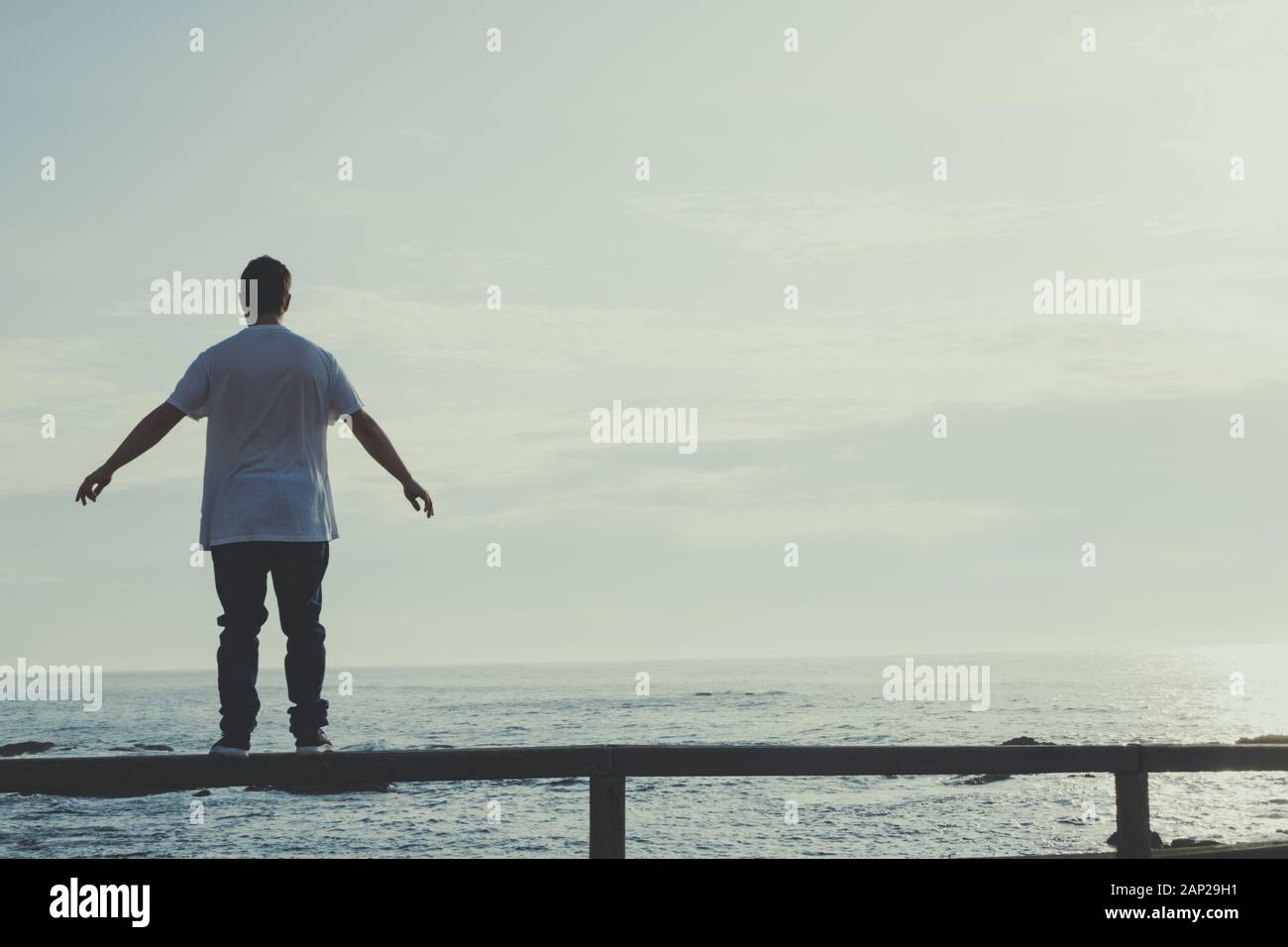 Mann mit ausgestreckten Armen auf einem Geländer am Meer Stockfoto