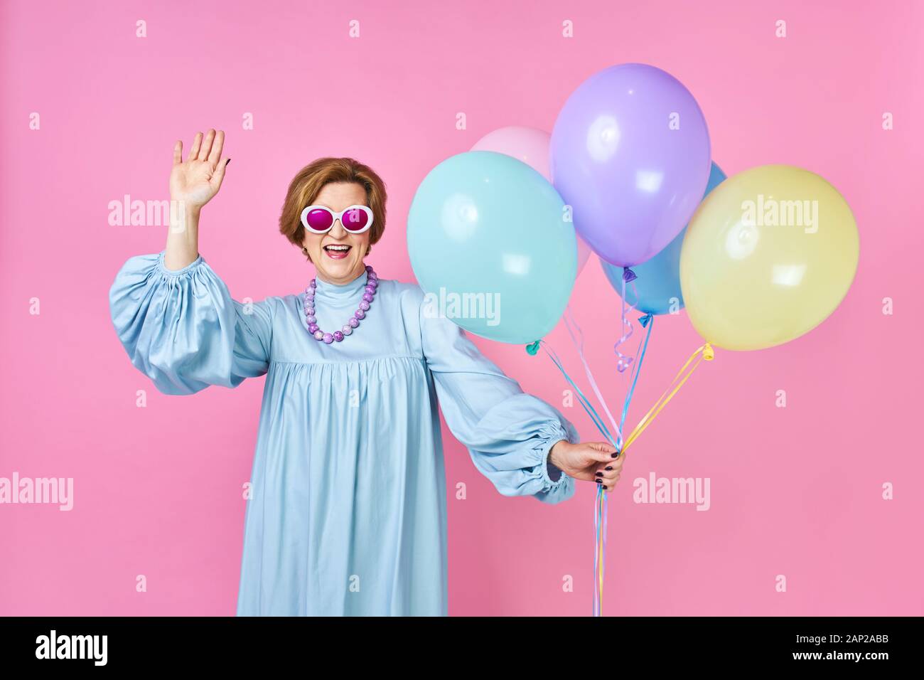 Nette alte Frau mit Luftballons in den blauen Anzug disco Dancer. Animator der Parteien für Kinder, lustige Clown auf einem rosa Hintergrund Stockfoto