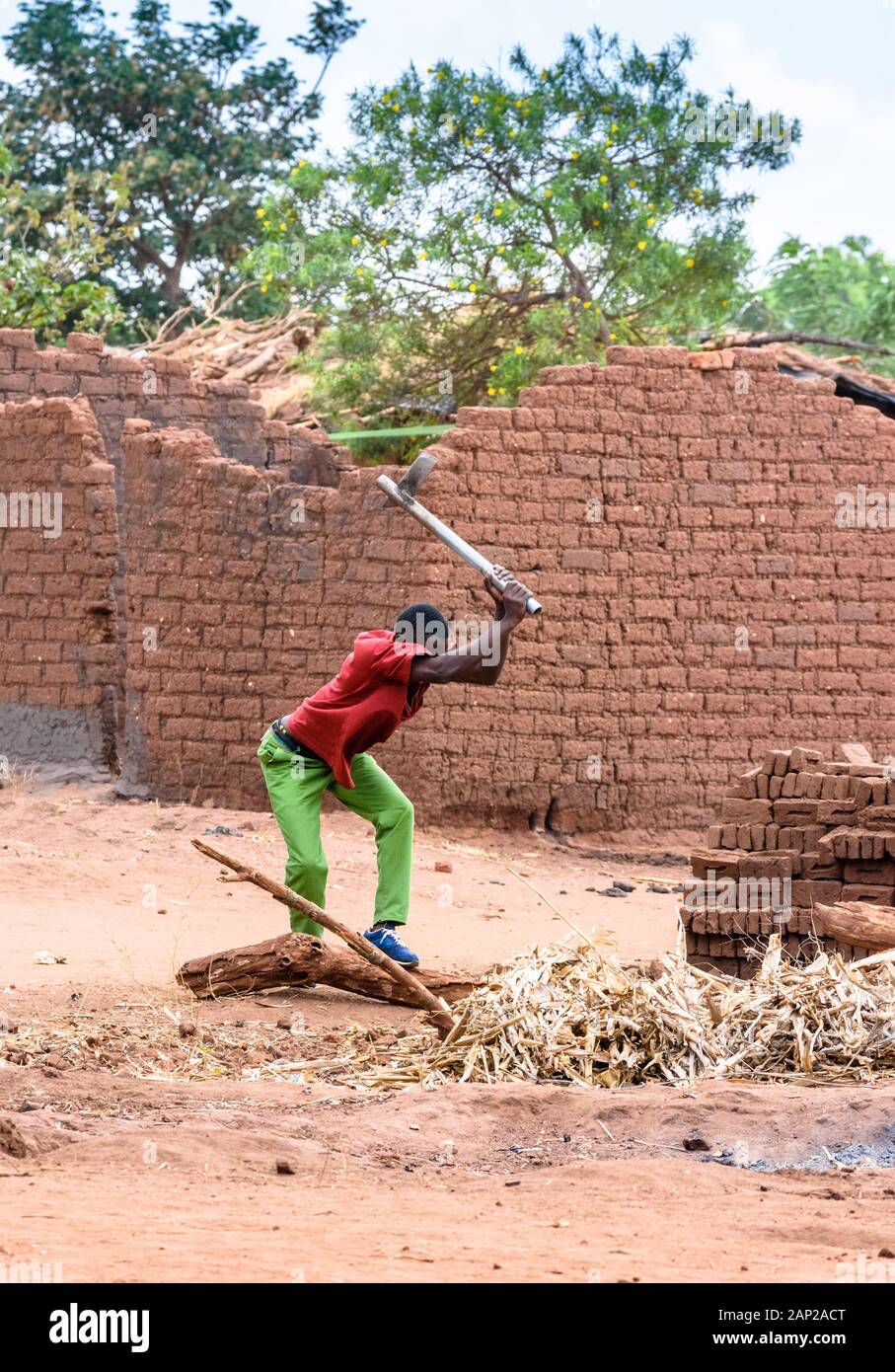 Ein malawischer Mann, der mit einer Axt Brennholz hackt, um in einem Dorf im Zentrum Malawis einen kleinen Ofen aus hausgemachten Backsteinen zu backen Stockfoto
