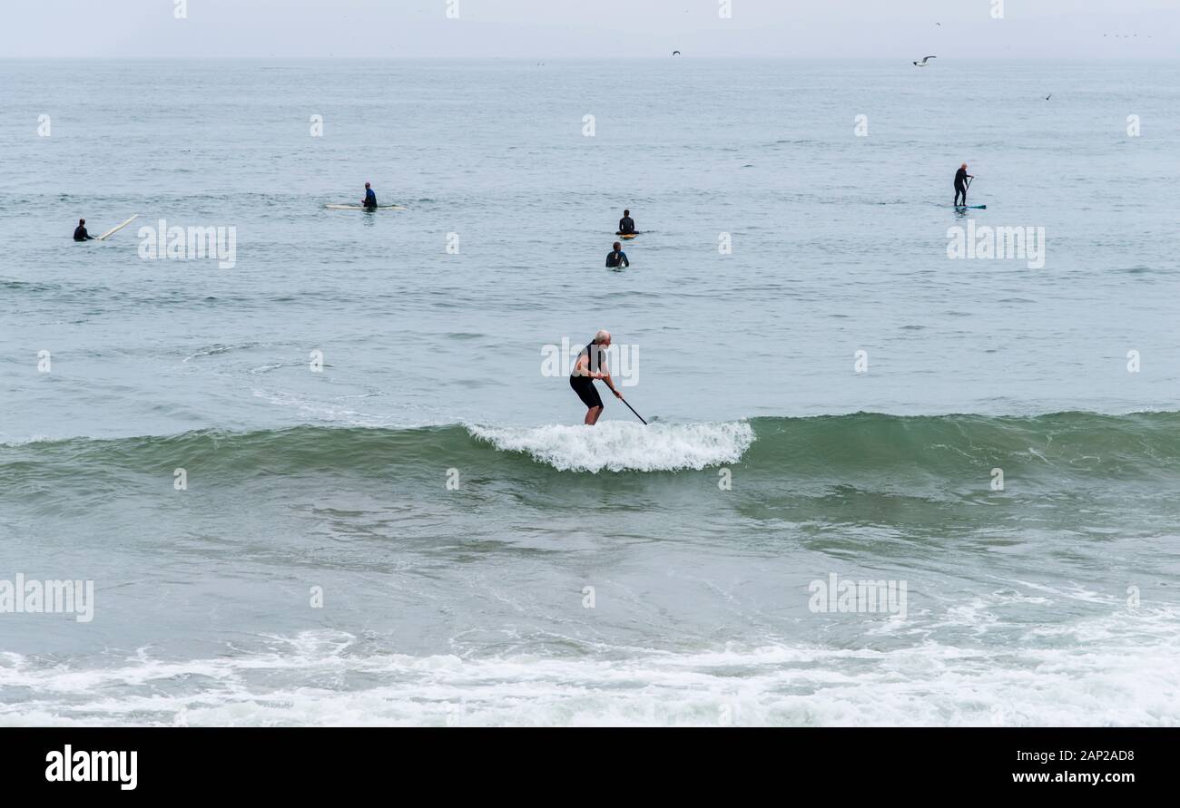 Surfer fangen glasige Pazifikwellen am Morro Rock Beach an einem übergiebelten Sommermorgen entlang der kalifornischen Küste. Stockfoto