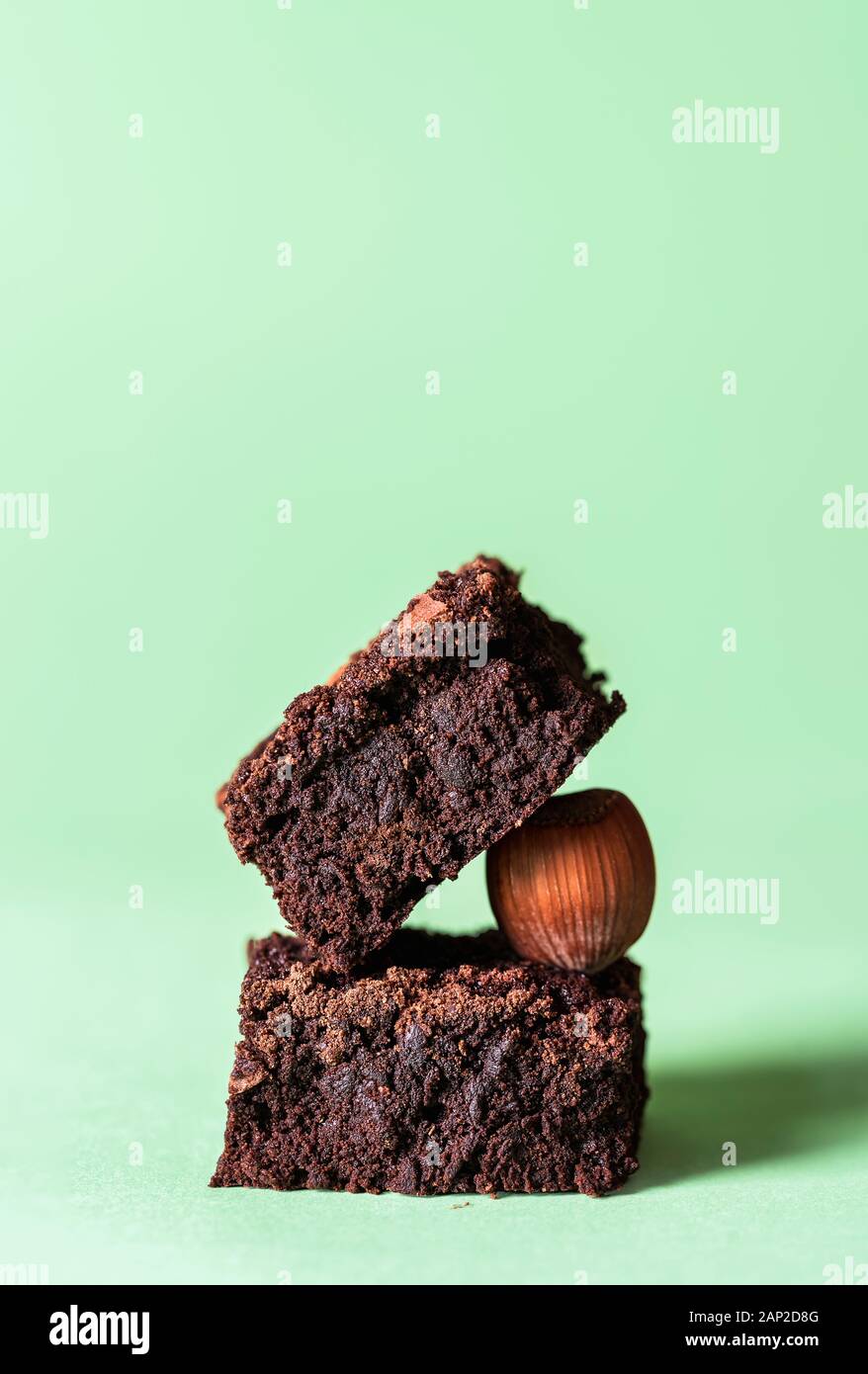 Stapel von zwei dunkle Schokolade brownies und eine Haselnuss, auf einem mint grün hinterlegt. Leckeres Fudge Chocolate Cake Squares. Ein netter Haufen von Brownies. Stockfoto