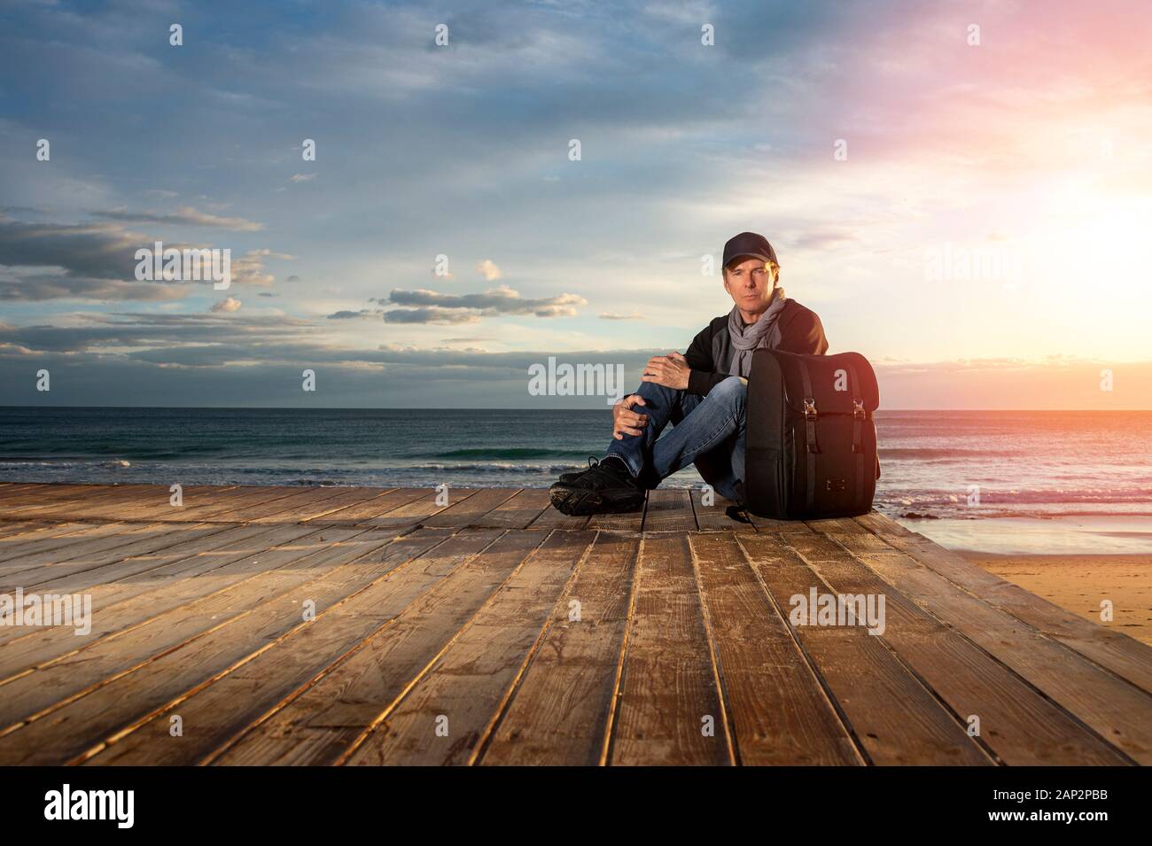 Der Mensch durch das Meer bei Sonnenuntergang mit einem Rucksack sitzend, in Richtung Kamera schaut. Stockfoto