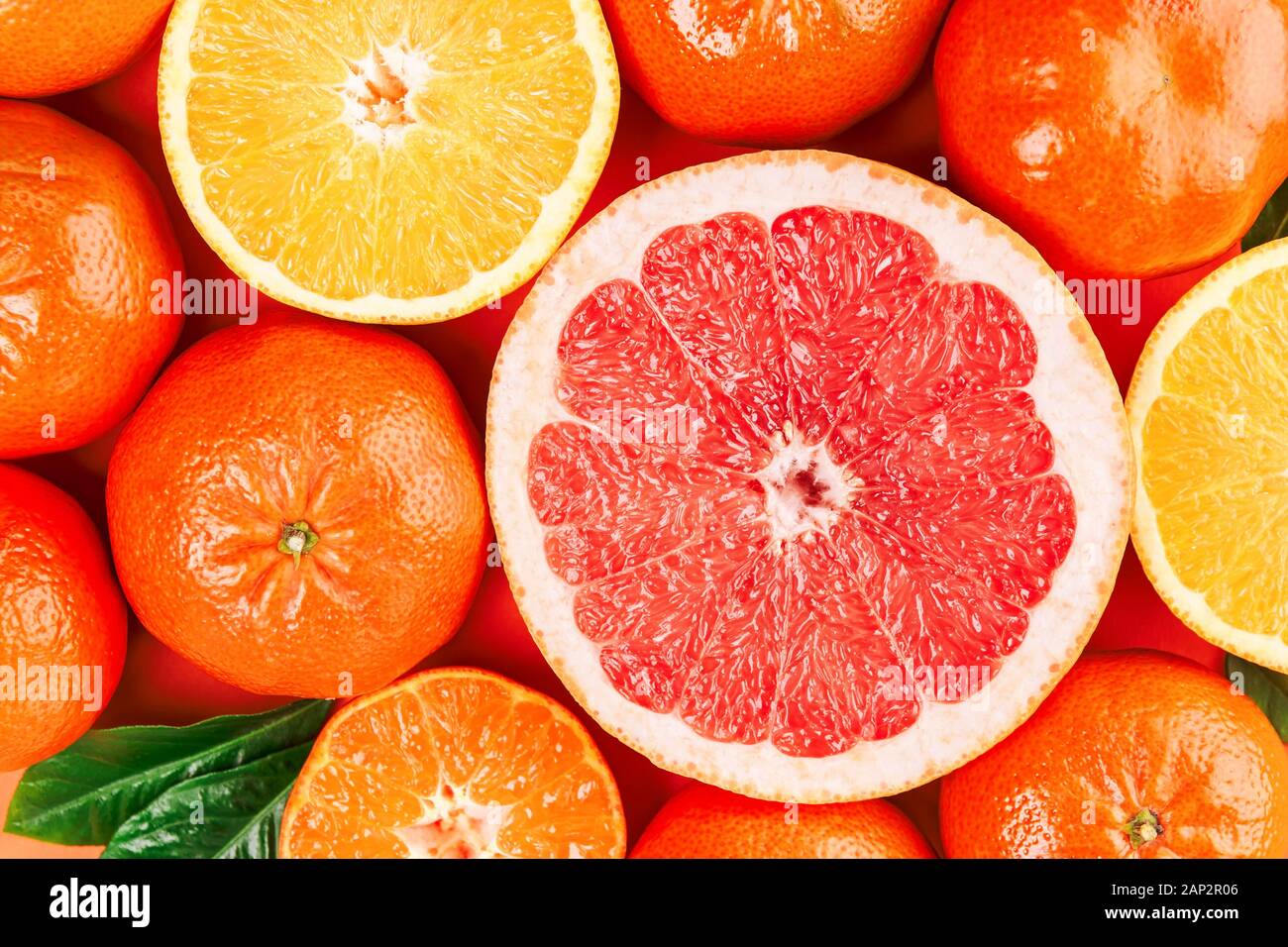 Frische reife Mandarinen, Grapefruits und Orangen mit grünen Blättern auf orangem Hintergrund. Nahaufnahme, Ansicht von oben. Stockfoto