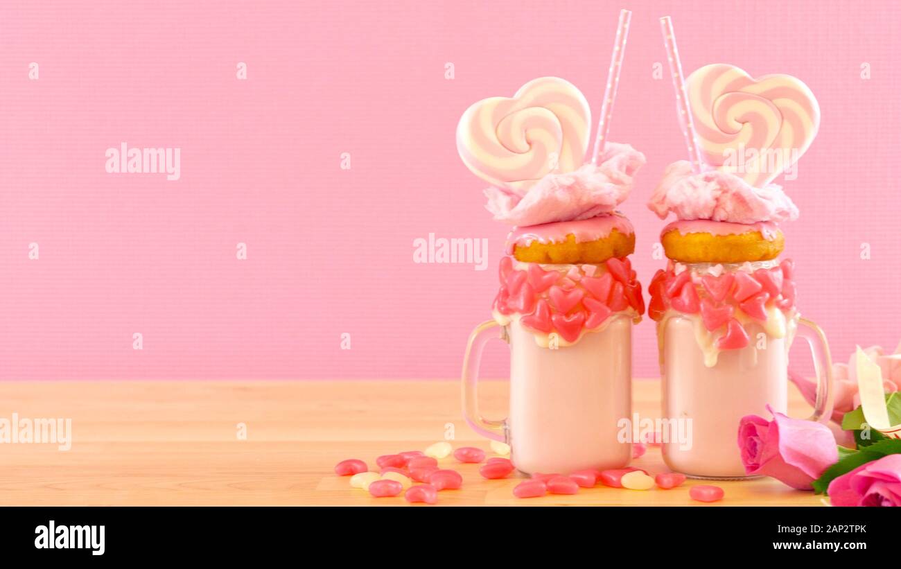 Auf dem Trend Valentinstag Tabelle Einstellung mit rosa Erdbeere freak Shakes mit herzförmigen Lutscher, Donuts und Zuckerwatte gekrönt. Negative Kopie sp Stockfoto