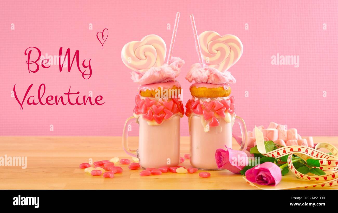 Auf dem Trend Valentinstag Tabelle Einstellung mit rosa Erdbeere freak Shakes mit herzförmigen Lutscher, Donuts und Zuckerwatte gekrönt, mit meinem Valen. Stockfoto
