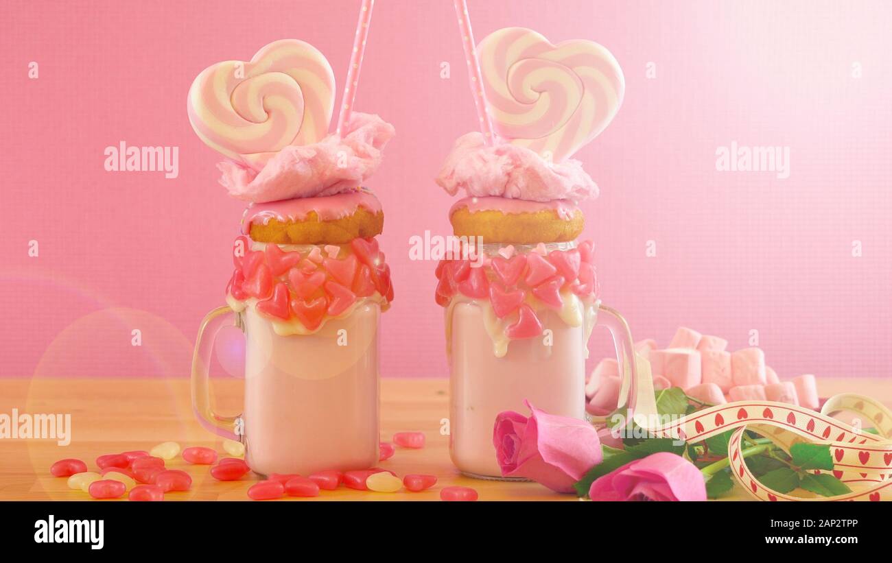 Auf dem Trend Valentinstag Tabelle Einstellung mit rosa Erdbeere freak Shakes mit herzförmigen Lutscher, Donuts und Zuckerwatte gekrönt, mit Lens Flare. Stockfoto