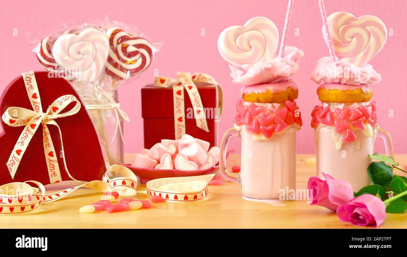 Auf dem Trend Valentinstag Tabelle Einstellung mit rosa Erdbeere freak Shakes mit herzförmigen Lutscher, Donuts und Zuckerwatte gekrönt. Stockfoto
