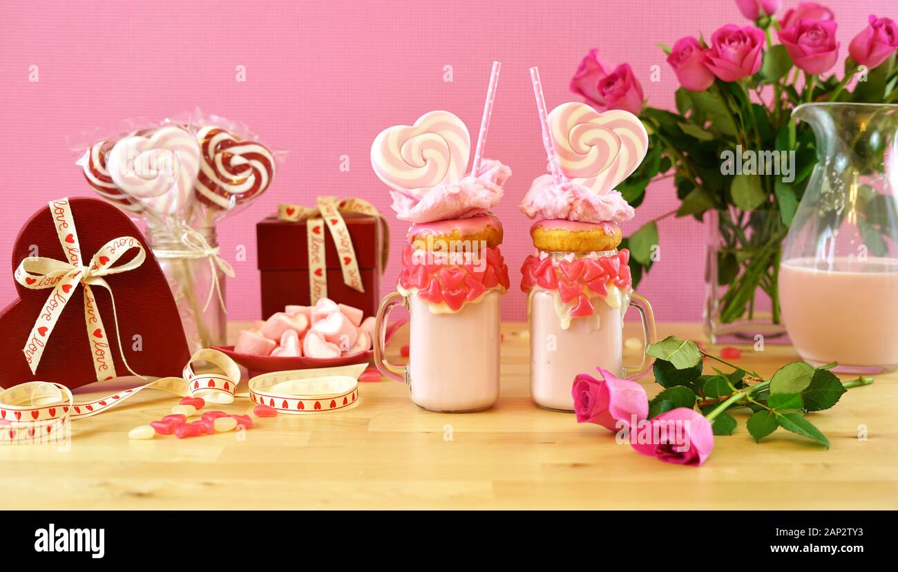 Auf dem Trend Valentinstag Tabelle Einstellung mit rosa Erdbeere freak Shakes mit herzförmigen Lutscher, Donuts und Zuckerwatte gekrönt. Große Ernte für Wir Stockfoto