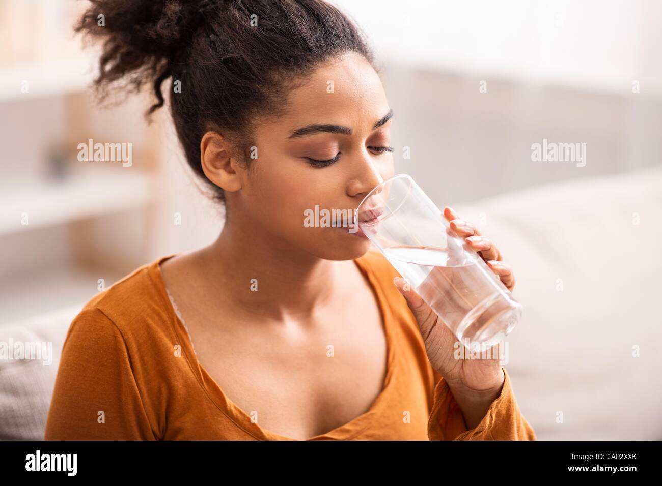 Junge Schwarze Lady Trinkwasser Sitzen auf der Couch zu Hause Stockfoto