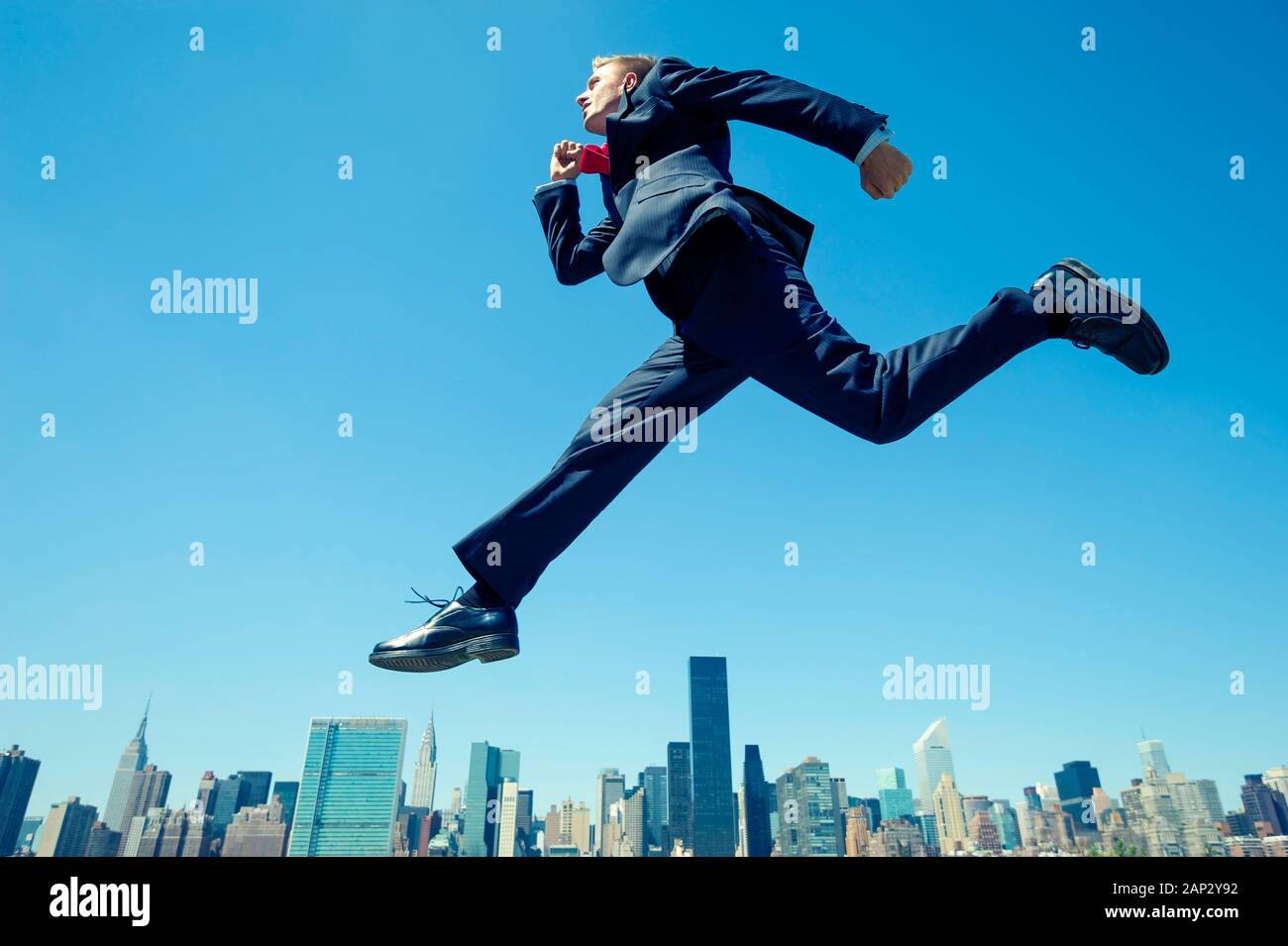 Riesige Geschäftsmann in hellen blauen Himmel über der Skyline der Stadt springen Stockfoto
