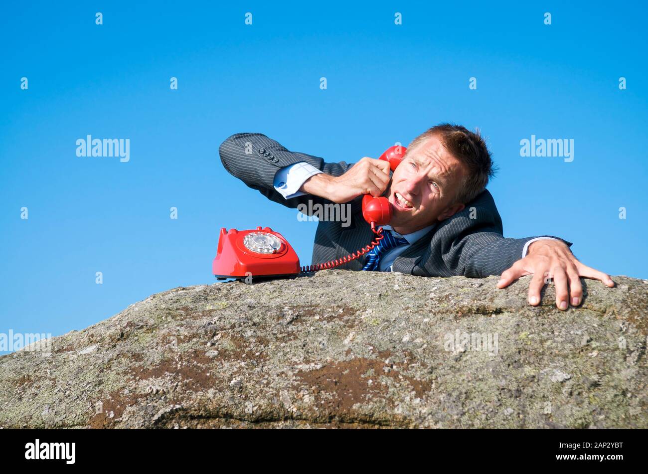 Geschäftsmann aus baumelt eine Felswand einen verzweifelten Anruf auf ein rotes Telefon Hotline Stockfoto