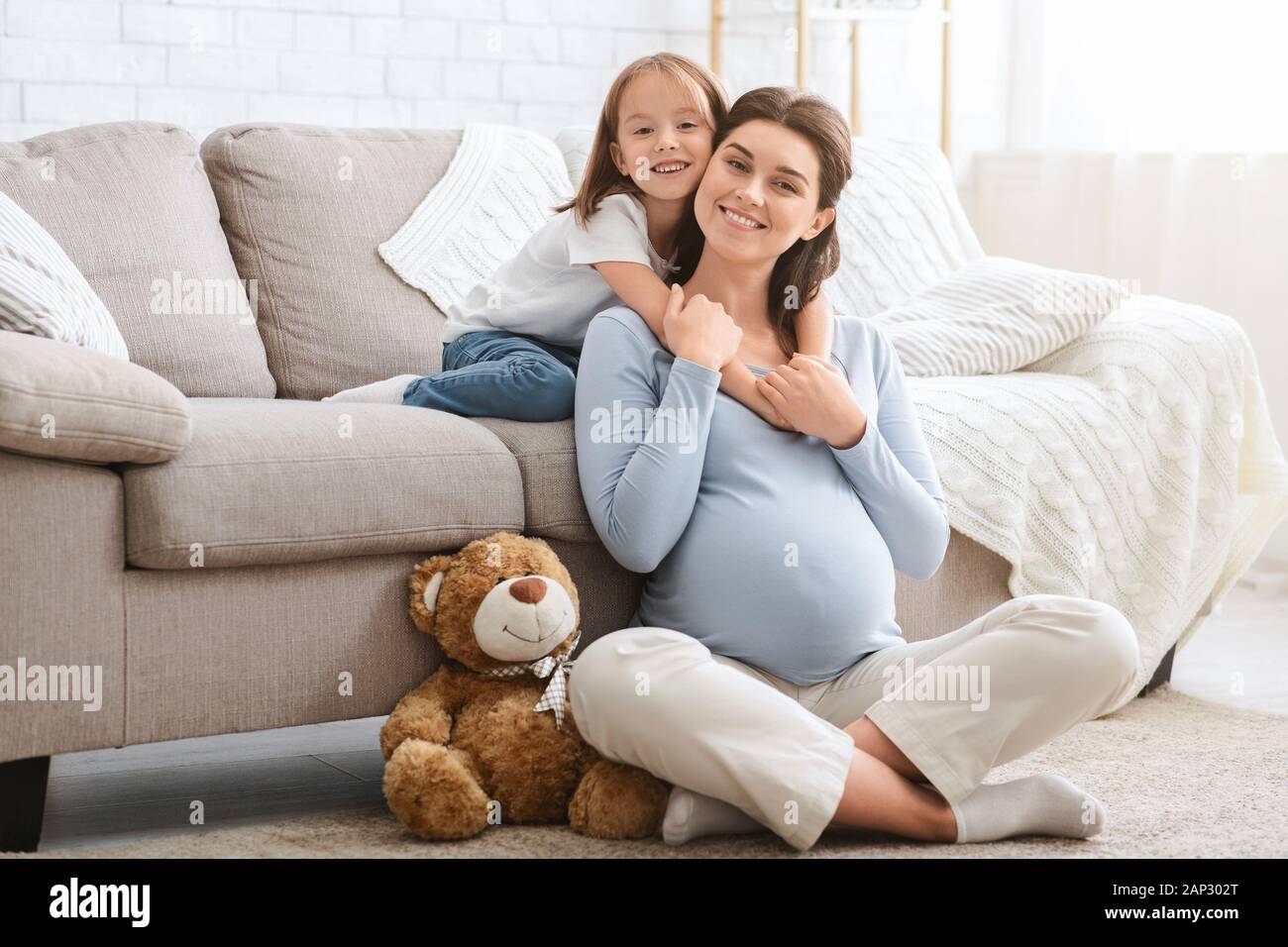 Lächelnd kleine Tochter umarmte ihre Mutter glücklich Schwanger Stockfoto