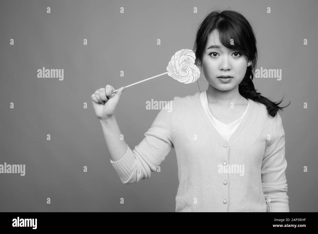 Junge schöne asiatische Frau mit herzförmigem Lollipop Stockfoto