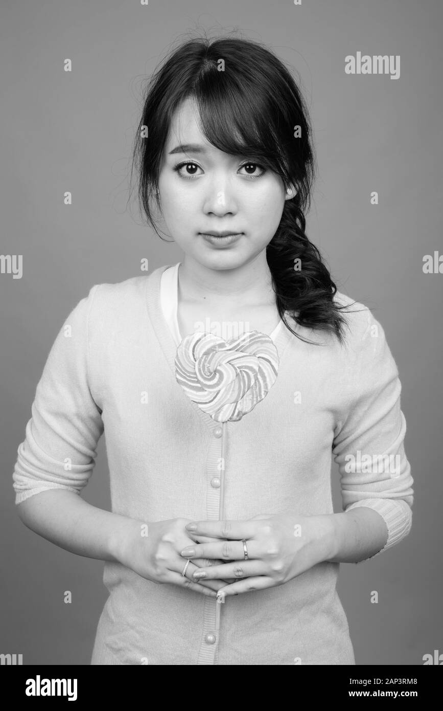 Junge schöne asiatische Frau mit herzförmigem Lollipop Stockfoto