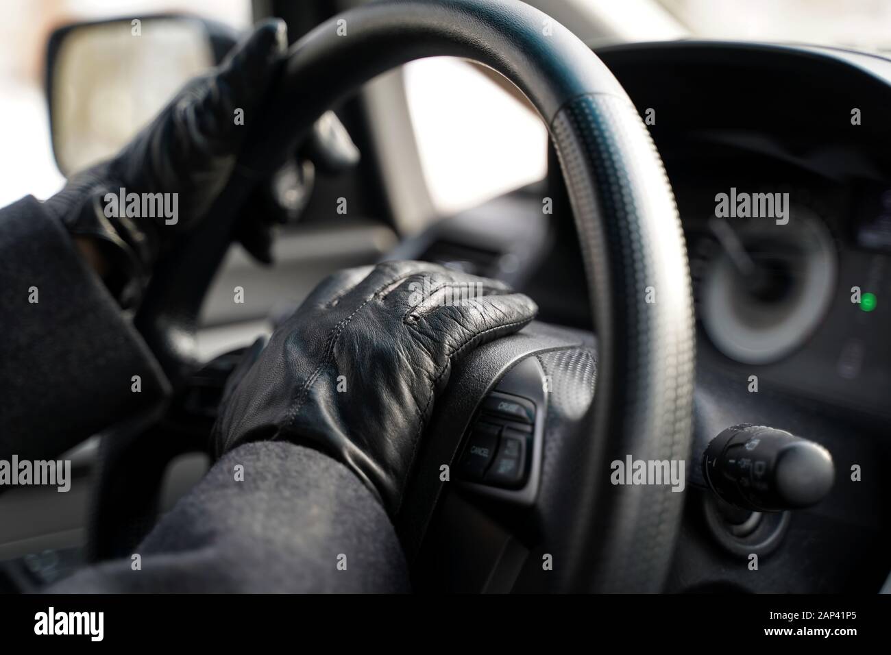 Hände in Lederhandschuhen mit Hupe fahren, indem man das Lenkrad des Fahrzeugs herunterdrückt. Stockfoto