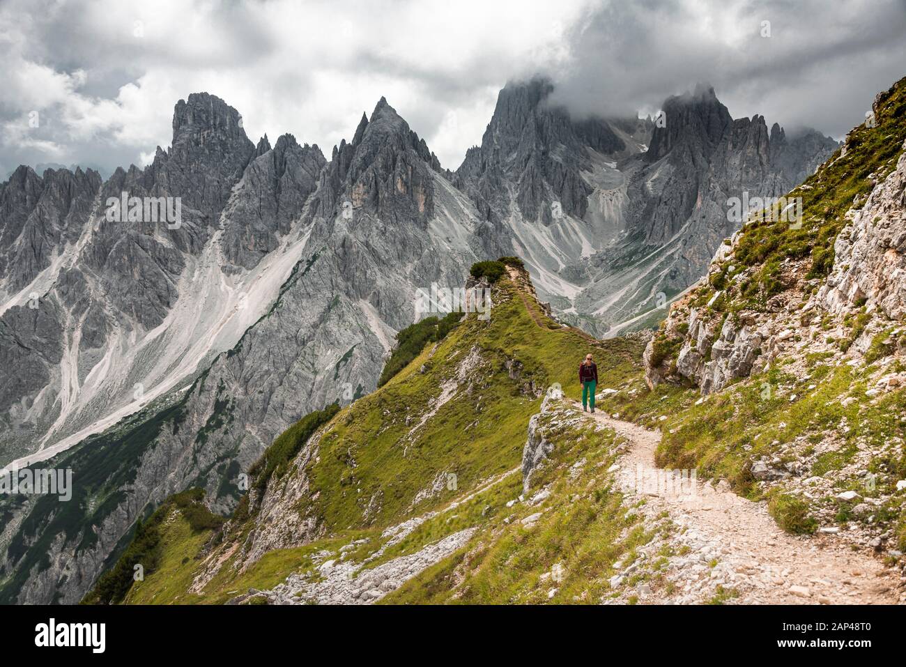 Junge Frau, Bergsteigerin auf einem Wanderweg, hinter Bergspitzen und steilen Felsgipfeln, dramatischen Wolken, Cimon di Croda Liscia und Cadini-Gruppe Stockfoto