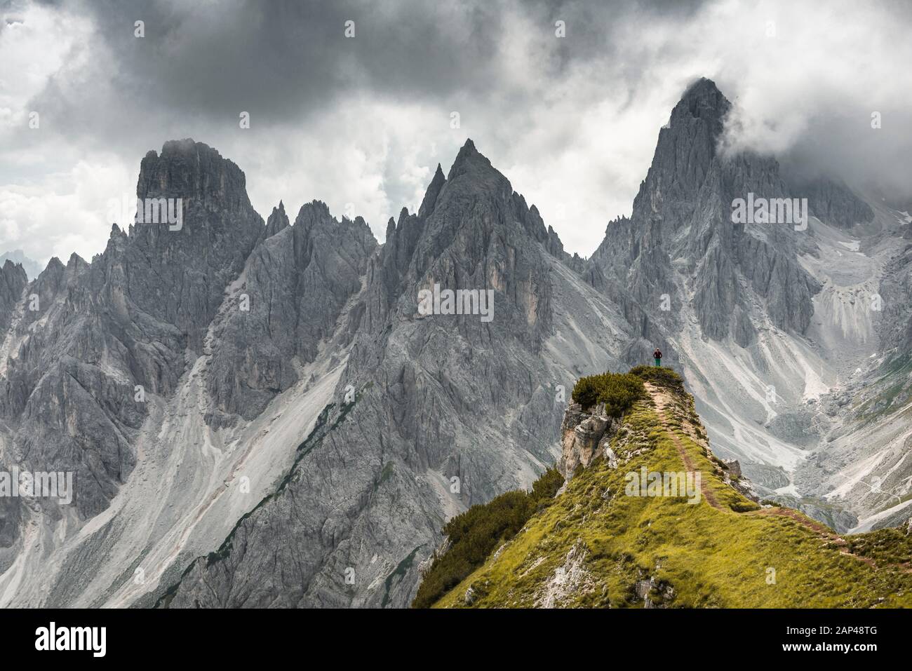 Frau, die auf einem Bergrücken, hinter Bergkuppen, Felsrücken mit scharfen Felsspitzen, dramatischen Wolken, Cimon di Croda Liscia und Cadini Group, Sesto, steht Stockfoto
