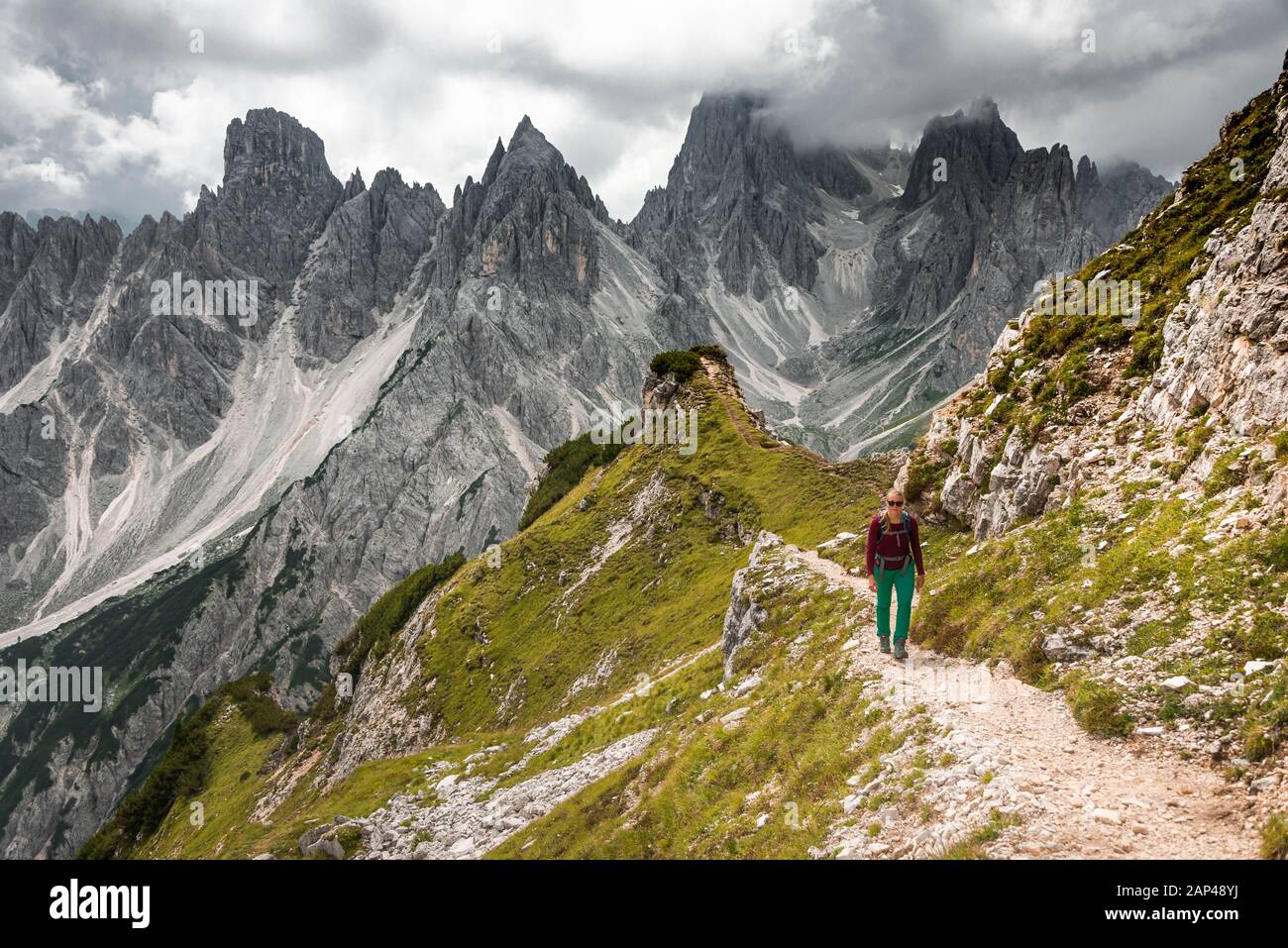 Junge Frau, Bergsteigerin auf einem Wanderweg, hinter Bergspitzen und steilen Felsgipfeln, dramatischen Wolken, Cimon di Croda Liscia und Cadini-Gruppe Stockfoto