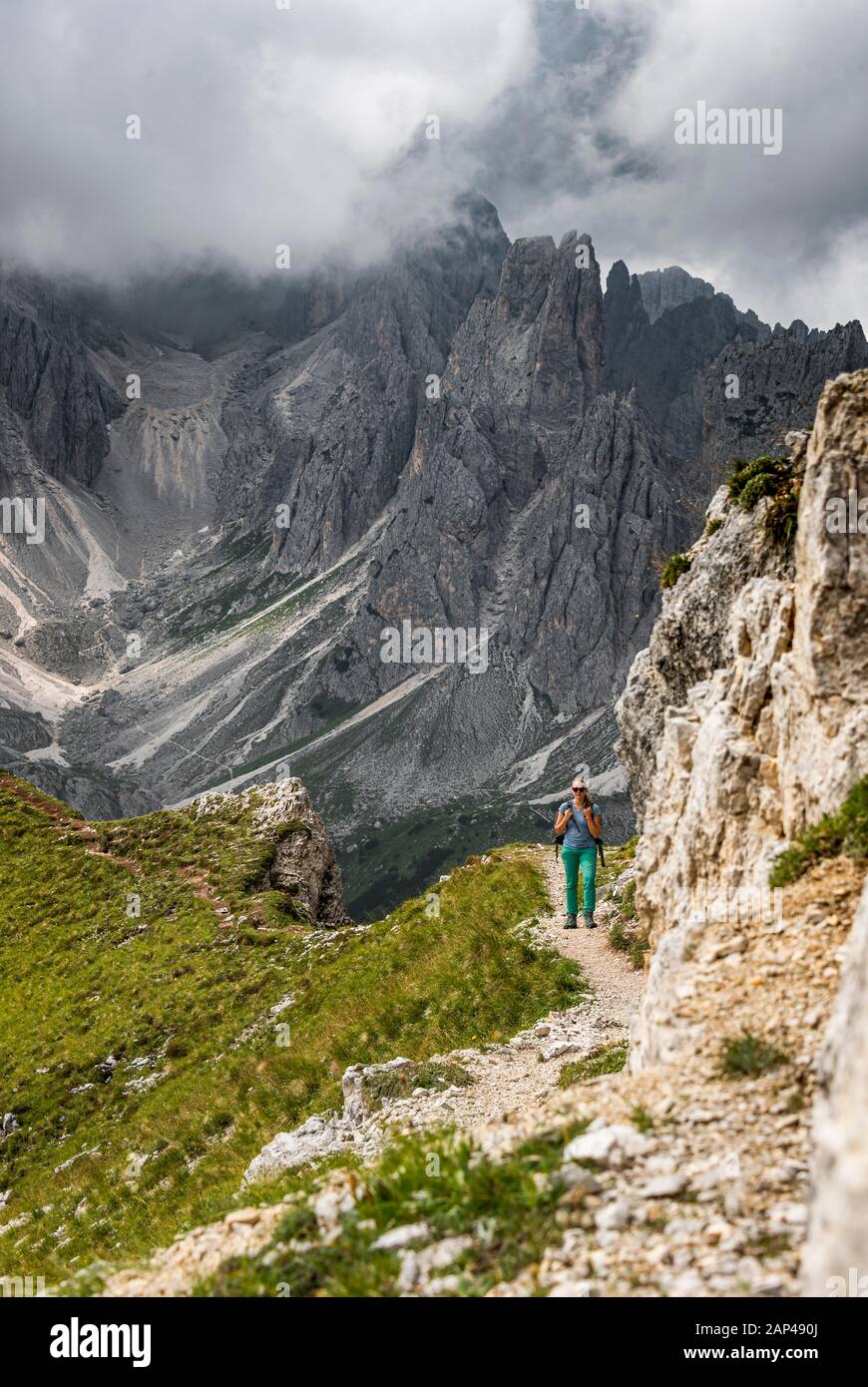 Junge Frau, Bergsteigerin auf einem Wanderweg, hinter Bergspitzen und steilen Felsgipfeln, bewölkter Himmel, Cimon di Croda Liscia und Cadini-Gruppe, Sexten Stockfoto