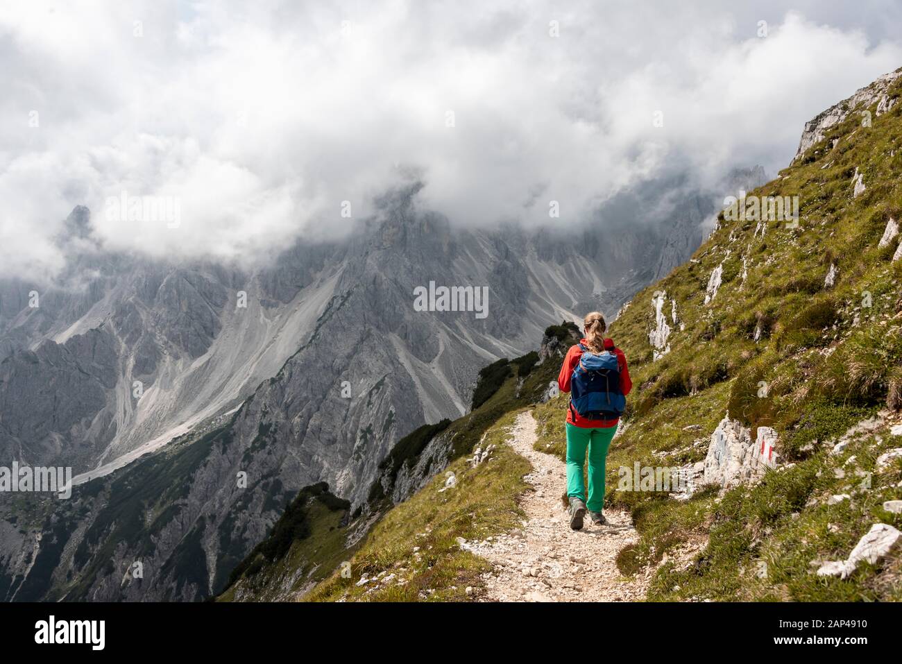 Junge Frau, Bergsteigerin auf einem Wanderweg, hinter Bergspitzen und steilen Felsgipfeln, bewölkter Himmel, Cimon di Croda Liscia und Cadini-Gruppe, Sexten Stockfoto