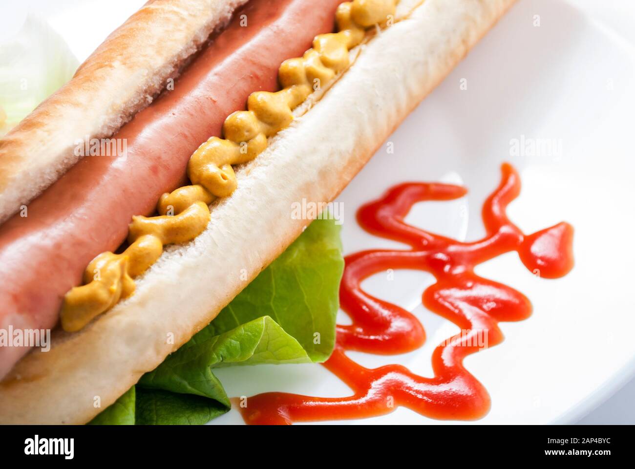 Hot Dog mit Senf und Ketchup auf weißem Teller. Nahaufnahme eines amerikanischen Hotdog. Schnellimbiss im Restaurant. Wiener Wurst mit Senf. Stockfoto