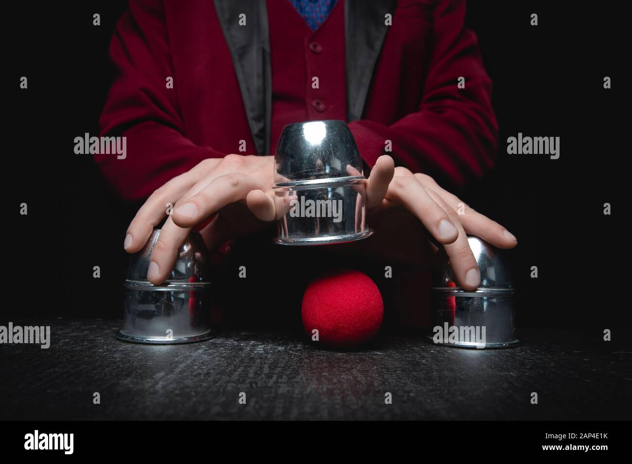Magier zeigt Schalenspiel von Thimbeln mit Kreisen und Ball, schwarzer Hintergrund. Konzept Täuschung, Schlittenhand Stockfoto