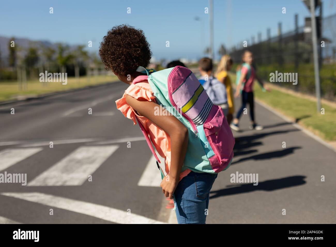 Schulkinder, die auf der Suche nach Verkehrsbehinderungen sind, während sie auf die Straße warten Stockfoto