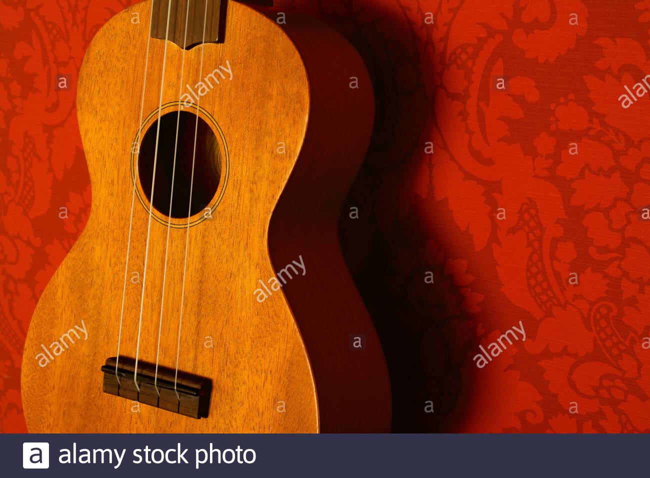 Nahaufnahme einer Ukulele mit honigfarbenem Holz vor rotem Tapetenhintergrund Stockfoto