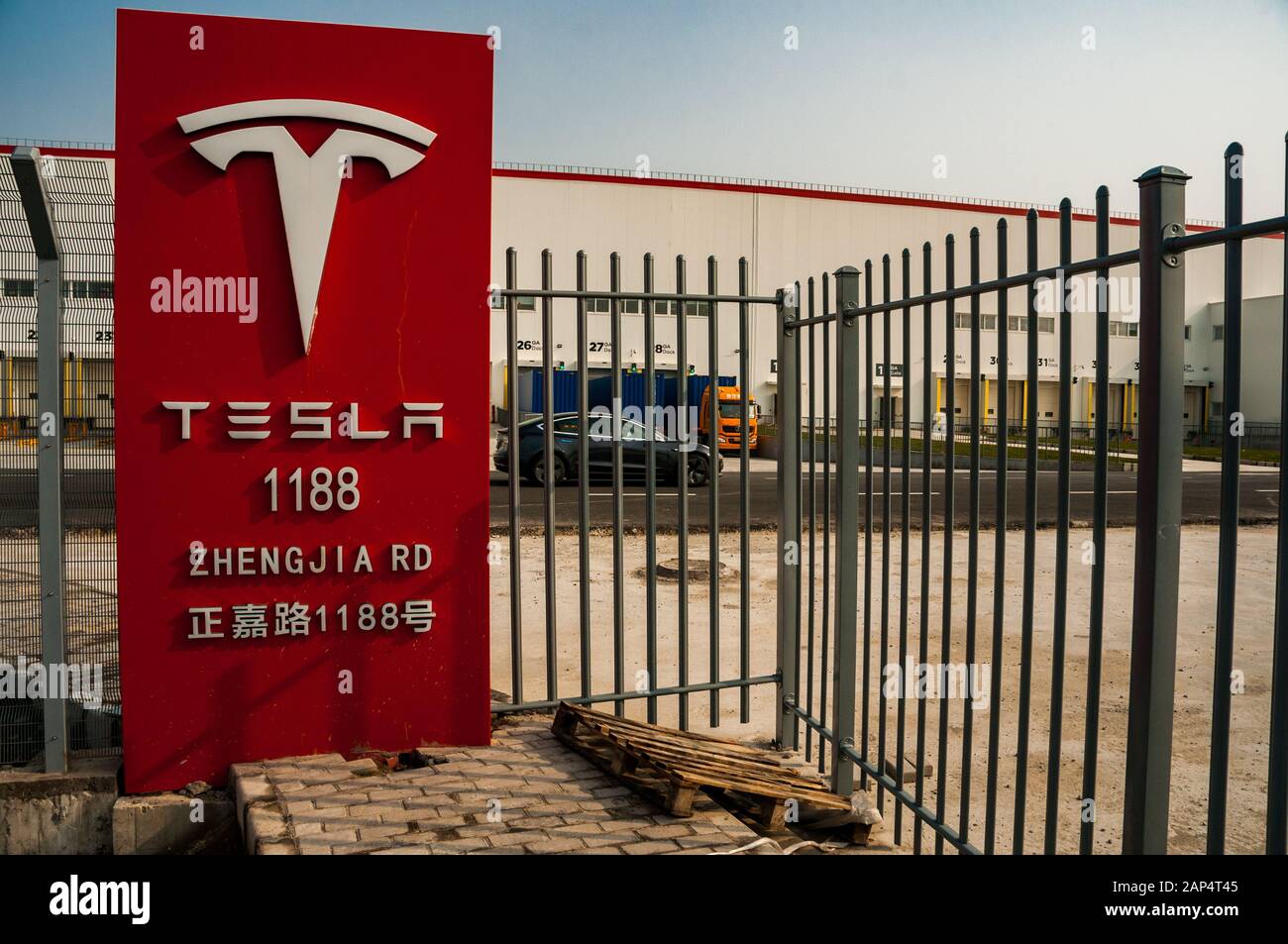 Tesla-Schild vor der chinesischen Fabrik mit einem Modell 3, das im Hintergrund vorbeifährt. Stockfoto