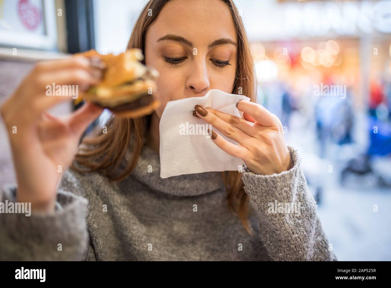 Schöne junge süße Mädchen in der Brücke reinigt den Mund nach einem großen Biss und geniesst fast food Hamburger während sittting in einem Café. Stockfoto