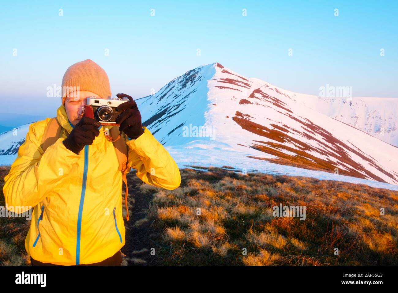 Fotograf in gelber Jacke unter Foto mit retro Kamera auf verschneiten Bergen Stockfoto