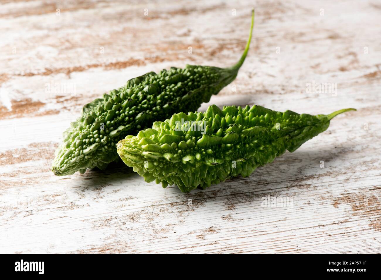 Einige Rohstoffe karela, auch als bitter Melone oder bitteren Kürbis bekannt, auf einem weißen rustikalen Holztisch Stockfoto
