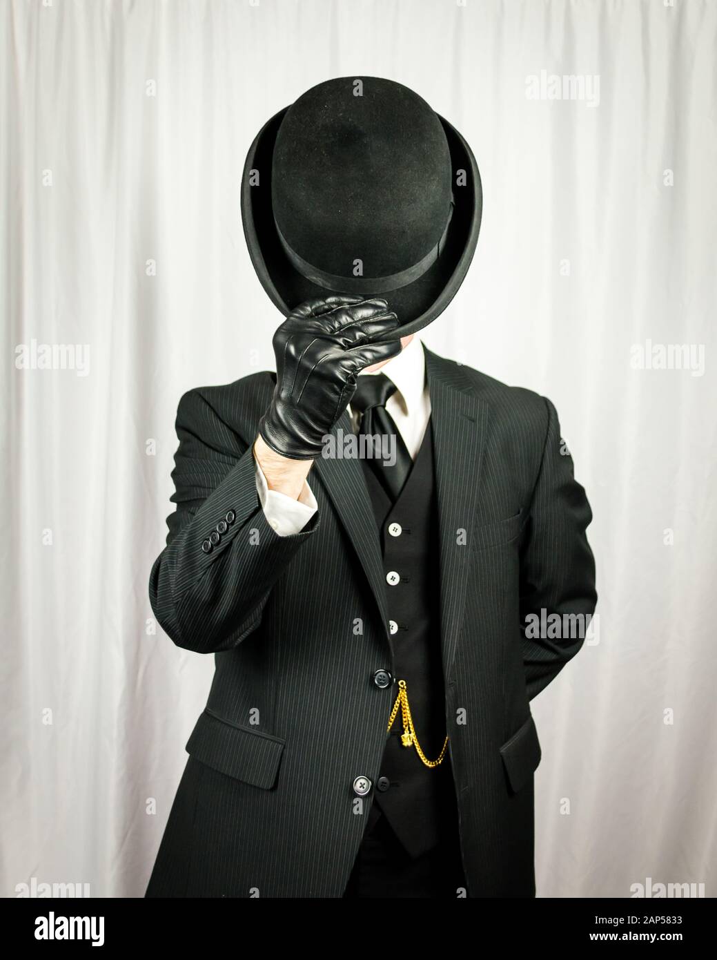 Porträt des erfolgreichen Mann in dunklen Anzug und Lederhandschuhe Doffing Bowler Hut. Konzept des klassischen und exzentrischen britischen Gentleman. Retro-Mode. Stockfoto