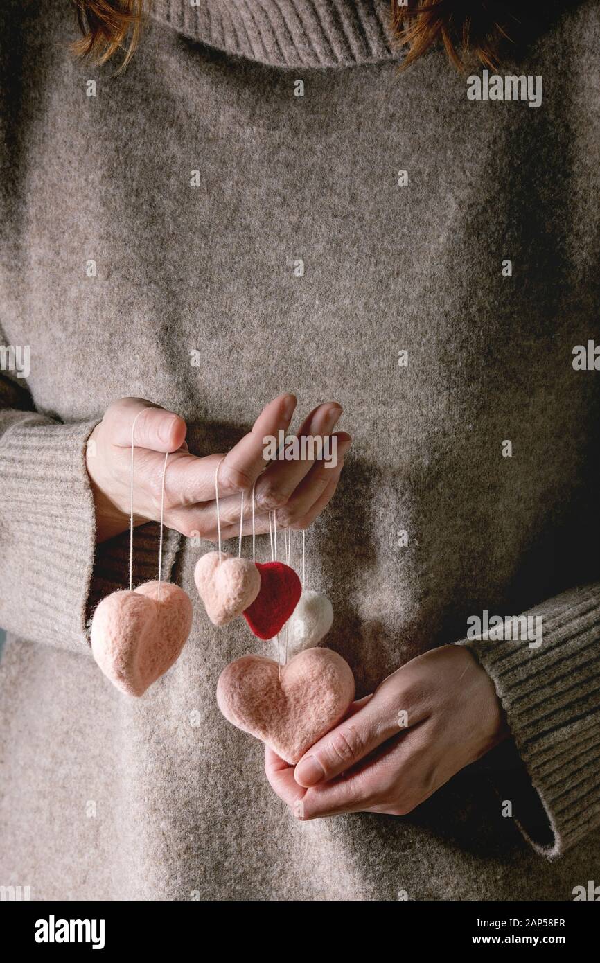 Frau in Kaschmir Pullover halten Sie in Händen der Nadel gefilzte Herzen auf den Gewinden. St Valentines Tag Grußkarte Stockfoto