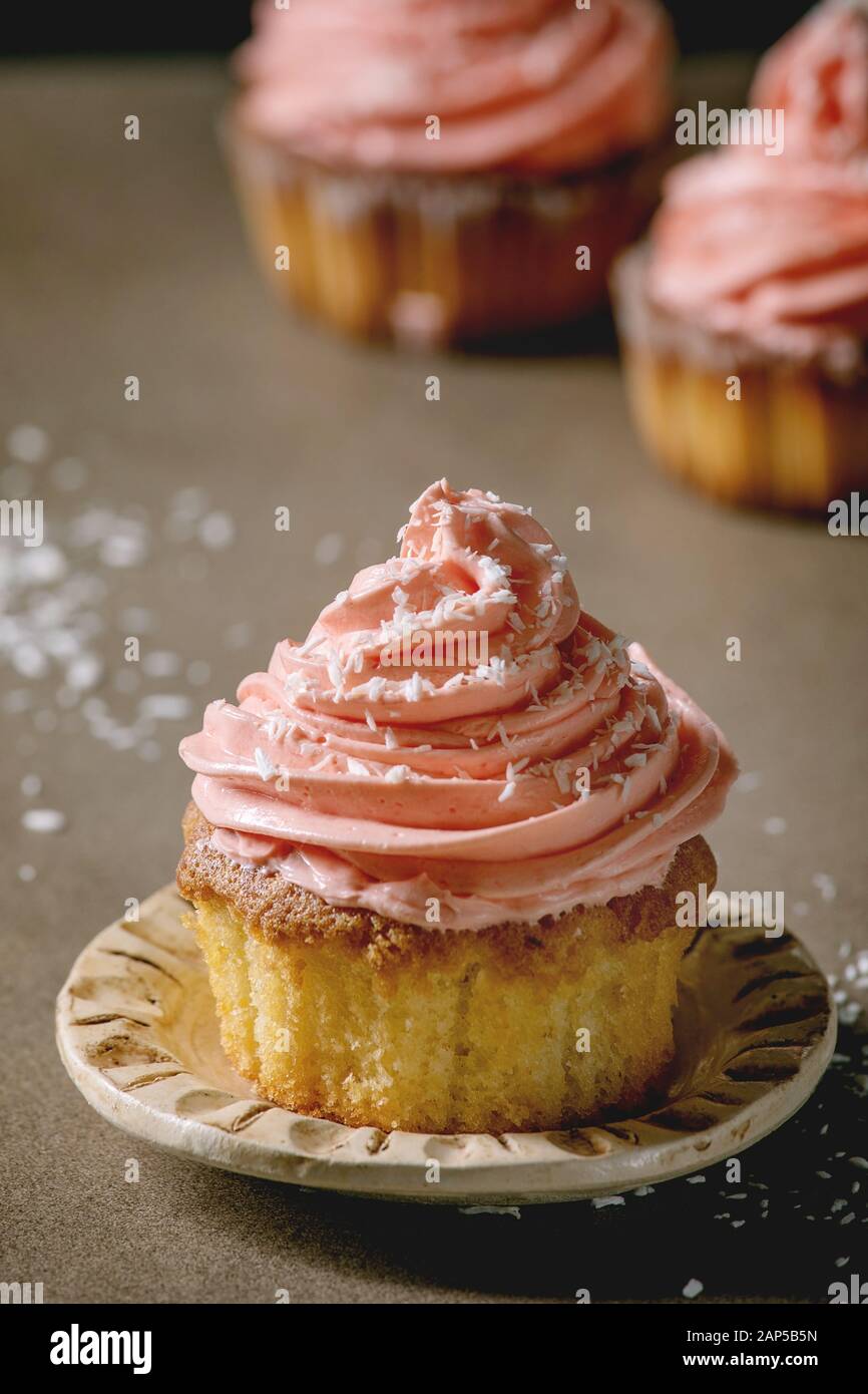 Hausgemachte Muffins mit Rosa buttercream und Kokosraspeln auf Keramikplatte auf dunklen Tisch serviert. Nahaufnahme Stockfoto