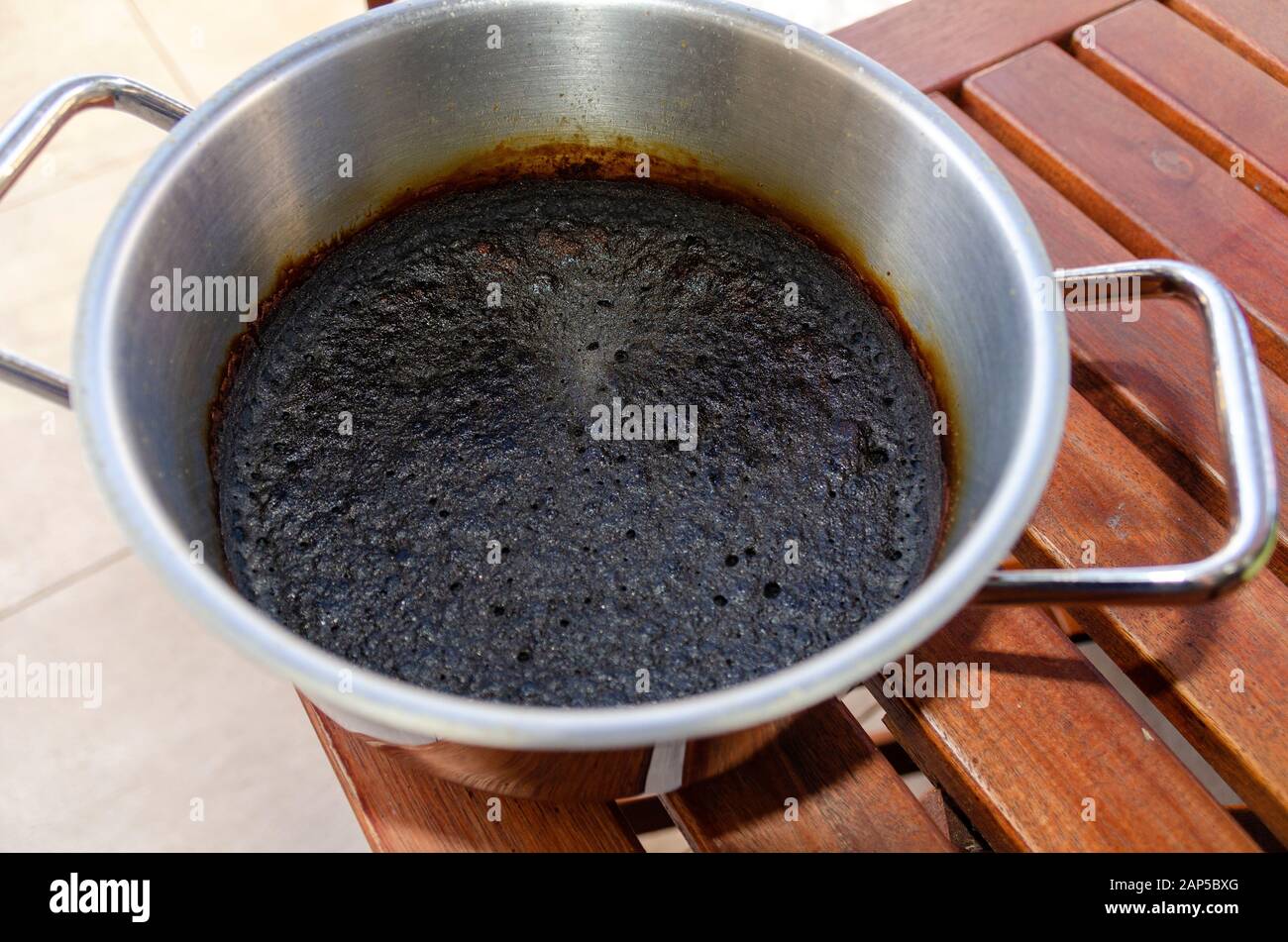 Metallischer Topf mit Lebensmitteln, der auf einem Holztisch zu einem Schlagader gebrannt wurde Stockfoto