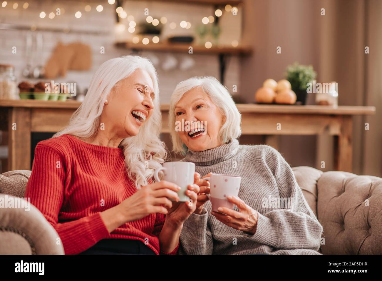 Zwei grauhaarige angenehm süßen Damen sitzen auf dem Sofa und schauen erstaunlich Stockfoto