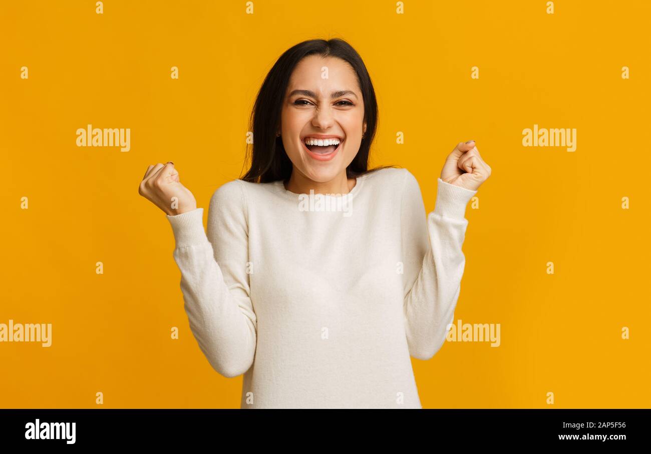 Ekstatisches hispanisches Mädchen, das emotional Erfolge über den gelben Hintergrund feiert Stockfoto