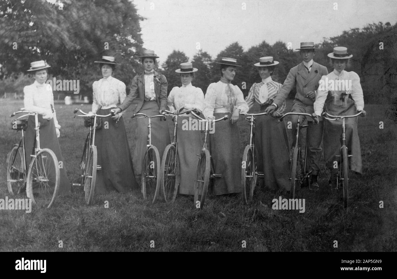 C 1900s, historisch, eine Gruppe von Damen, die Strohboaterhüte und lange Kleider tragen, die auf einem Feld mit ihren Fahrrädern zusammenstehen, England, Großbritannien. In dieser Epoche war das Fahrradfahren eine beliebte Freizeitaktivität für Erwachsene, und ihre Maschinen wurden als "sichere" Fahrräder bezeichnet, da die Räder im Vergleich zu den hohen Rädern oder Penny-Farthings des späten viktorianischen Zeitalters und ihren Luftreifen niedriger waren. Die Erfindung des Sicherheitsfahrrades war eine radikale Entwicklung für Frauen, die die Freiheit außerhalb des Wohnbereichs gab und eine Schlüsselrolle bei ihrer Befreiung spielte, da sie ihnen persönliche Mobilität und Unabhängigkeit verschaffte. Stockfoto